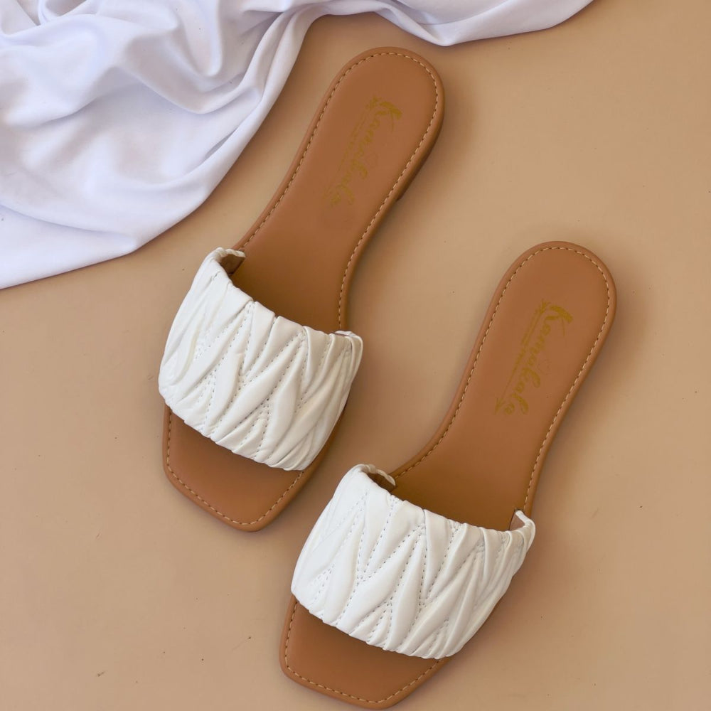Pair of white textured slippers on a beige surface with a white fabric background